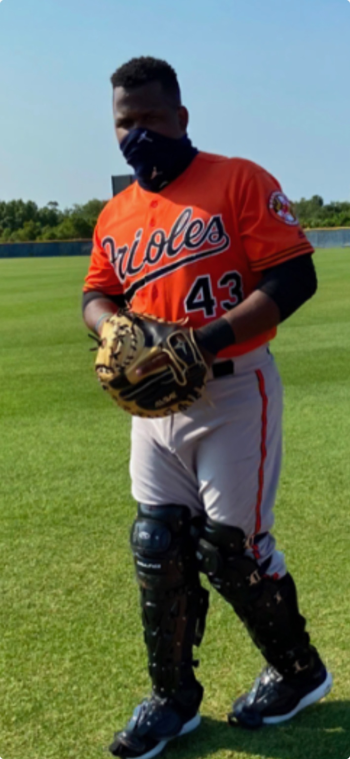 Coach Deiby Ramírez in catcher's gear on a baseball field